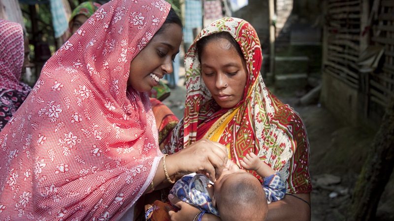 A health assistant working as vaccinator gives polio drops to a child during a house-to-house campaign.